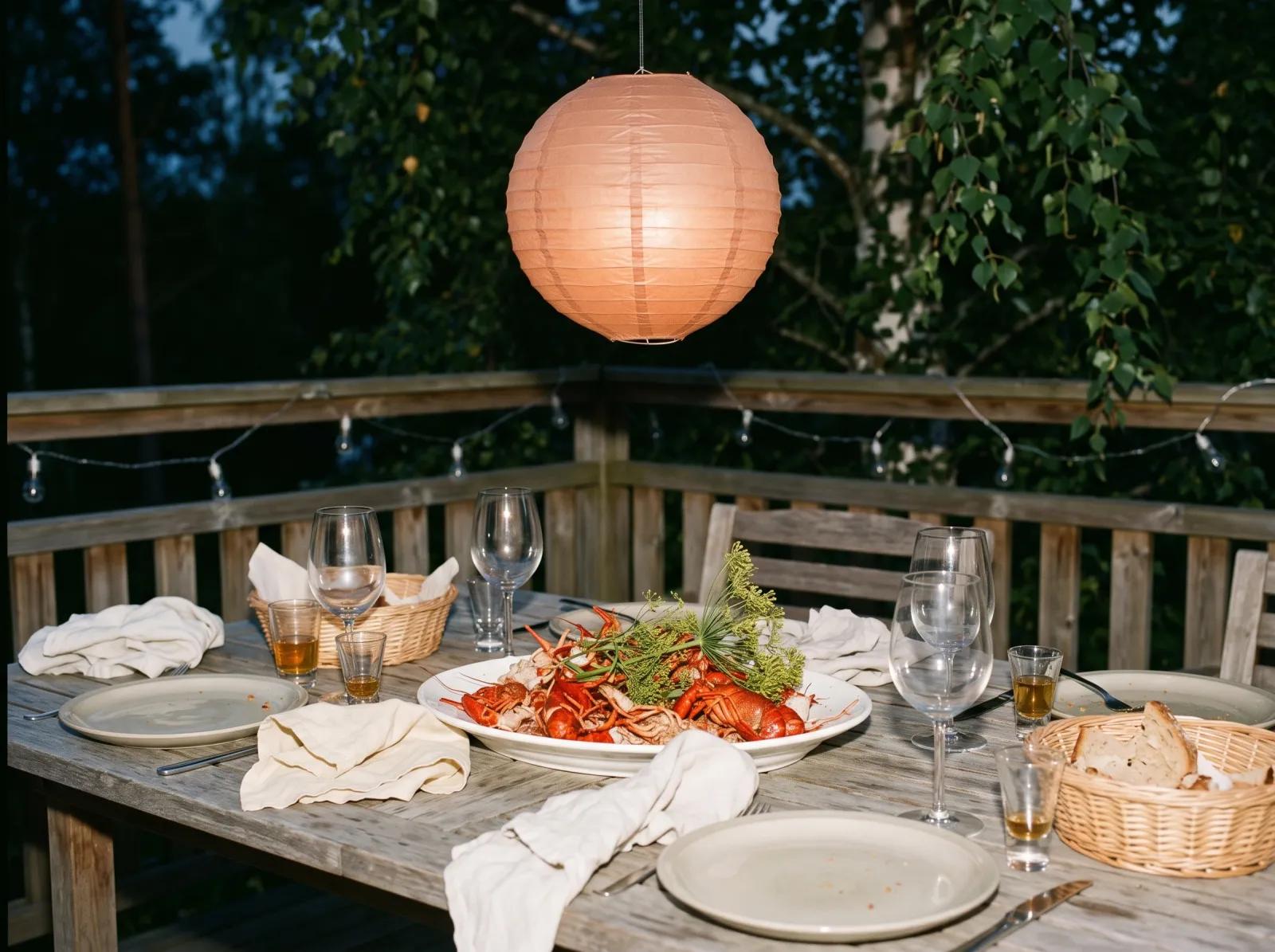 Kräftskiva på en altan i augustiskymning, med kräftfat, dill och en terrakottafärgad papperslykta över bordet.